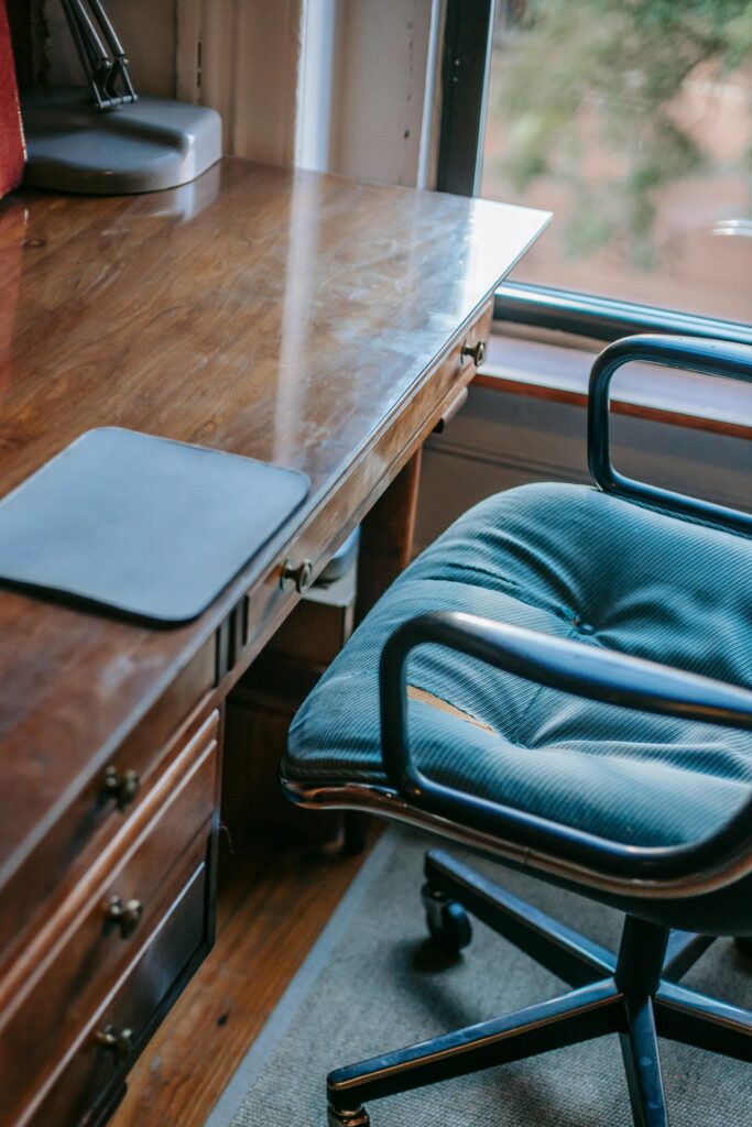 From above of domestic workplace in retro style with graphic tablet pad placed on old fashioned wooden table with drawers and soft armchair